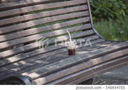 Plastic cup with leftover iced coffee on an old wooden park bench Plastic cup with leftover iced coffee on an old wooden park bench 140934785