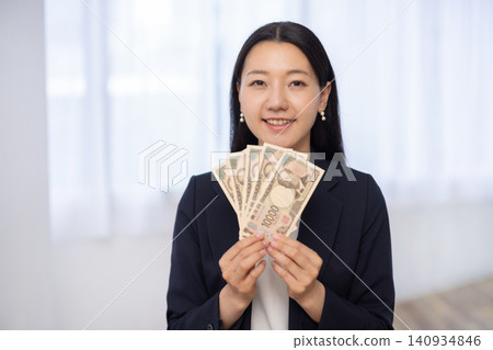A young Japanese businesswoman smiles at the camera, holding five 10,000 yen bills. A young Japanese businesswoman smiles at the camera, holding five 10,000 yen bills. 140934846