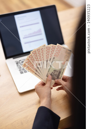 A close-up of a woman's hands as she counts out 10,000 yen bills. A close-up of a woman's hands as she counts out 10,000 yen bills. 140935223