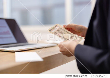 A close-up of a woman's hands as she counts out 10,000 yen bills. A close-up of a woman's hands as she counts out 10,000 yen bills. 140935230