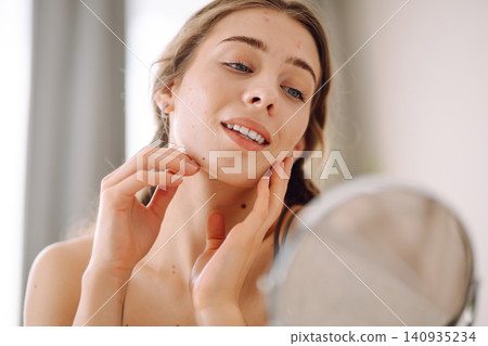 Young woman with problem skin looking into mirror. Inflammation on face, problem skin. Beauty care. Young woman with problem skin looking into mirror. Inflammation on face, problem skin. Beauty care. 140935234
