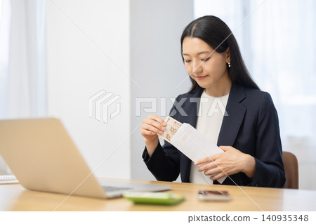 A young Japanese woman takes a 10,000 yen bill out of an envelope at her desk. 140935348