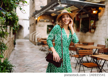 Young beautiful woman in trendy summer dress posing in street. Fashion style. Tourist attraction. Young beautiful woman in trendy summer dress posing in street. Fashion style. Tourist attraction. 140935541