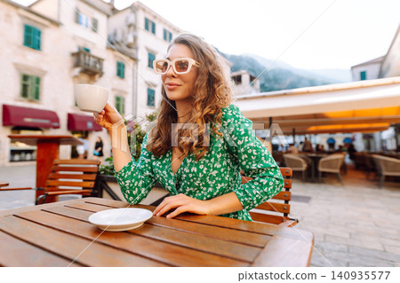 Happy woman sitting by table drinking coffee of outdoor sidewalk cafe restaurant, on summer day. Happy woman sitting by table drinking coffee of outdoor sidewalk cafe restaurant, on summer day. 140935577