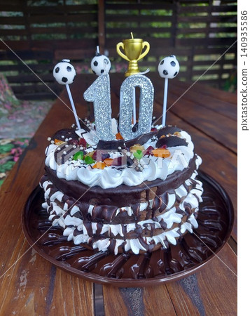 A beautifully decorated chocolate cake adorned with whipped cream and candies, set on a wooden surface, possibly an outdoor table, creating a celebratory atmosphere with a top-down view ofa. A beautifully decorated chocolate cake adorned with whipped cream and candies, set on a wooden surface, possibly an outdoor table, creating a celebratory atmosphere with a top-down view ofa. 140935586