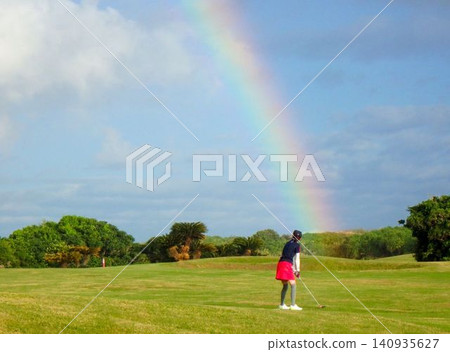 A female golfer plays a round of golf at a course with a beautiful rainbow overhead. 140935627