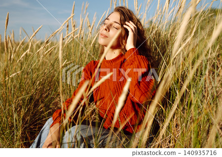 Beautiful young woman enjoying nature outdoors in tall grass. Flying hairs. Lifestyle. Fashion style Beautiful young woman enjoying nature outdoors in tall grass. Flying hairs. Lifestyle. Fashion style 140935716