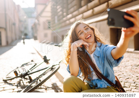 Happy woman using mobile phone while walks with a bicycle and looks around at beautiful architecture Happy woman using mobile phone while walks with a bicycle and looks around at beautiful architecture 140935897