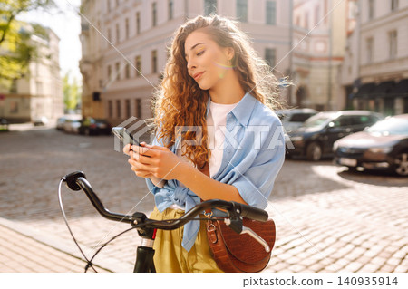 Woman using mobile phone, walks with bicycle, looks around at beautiful architecture. Selfie time. Woman using mobile phone, walks with bicycle, looks around at beautiful architecture. Selfie time. 140935914