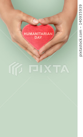 Top view of hands holding a red heart with the text HUMANITARIAN DAY on a green background, with copy space Top view of hands holding a red heart with the text HUMANITARIAN DAY on a green background, with copy space 140935939