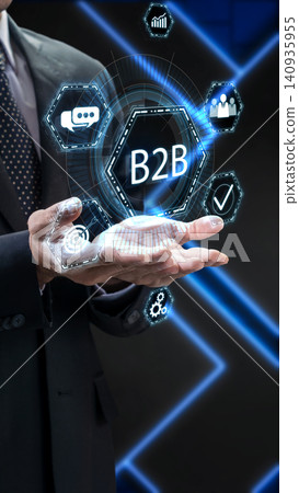 A businessman holds a glowing blue holographic B2B interface featuring business development icons, representing digital commerce and strategic networking A businessman holds a glowing blue holographic B2B interface featuring business development icons, representing digital commerce and strategic networking 140935955
