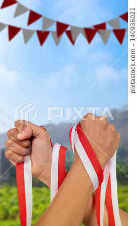 Two raised clenched fists wrapped in Indonesian red and white ribbon celebrating Independence Day under a blue sky. Hari Kemerdekaan, Merdeka, and Dirgahayu Indonesia on 17 Agustus Two raised clenched fists wrapped in Indonesian red and white ribbon celebrating Independence Day under a blue sky. Hari Kemerdekaan, Merdeka, and Dirgahayu Indonesia on 17 Agustus 140936021