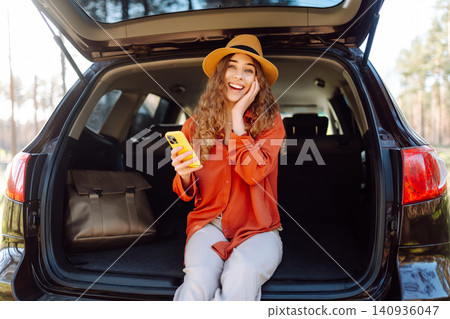Beautiful woman sits in the trunk of a car outdoor and uses a smartphone. Active life. 140936047
