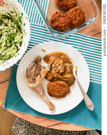 A person enjoys amaranth porridge with a boiled chicken leg, carrot meatballs, and fresh salad on a wooden table. The meal is placed on a striped mat with a bowl of salad nearby A person enjoys amaranth porridge with a boiled chicken leg, carrot meatballs, and fresh salad on a wooden table. The meal is placed on a striped mat with a bowl of salad nearby 140936100