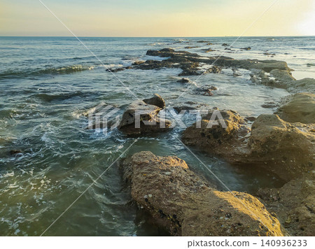 Golden hour light illuminates a rugged path of rocks leading into the calm ocean. This serene seascape symbolizes strength and tranquility, ideal for travel, wellness, and nature projects. Golden hour light illuminates a rugged path of rocks leading into the calm ocean. This serene seascape symbolizes strength and tranquility, ideal for travel, wellness, and nature projects. 140936233