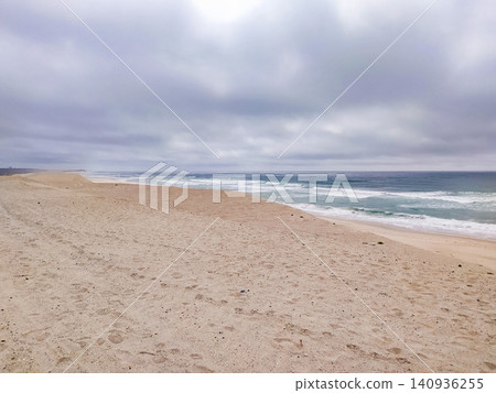 A vast, empty sandy beach stretches under a dramatic, overcast sky with rolling ocean waves crashing on the shore, evoking a powerful sense of solitude, peace, and wild coastal beauty. A vast, empty sandy beach stretches under a dramatic, overcast sky with rolling ocean waves crashing on the shore, evoking a powerful sense of solitude, peace, and wild coastal beauty. 140936255