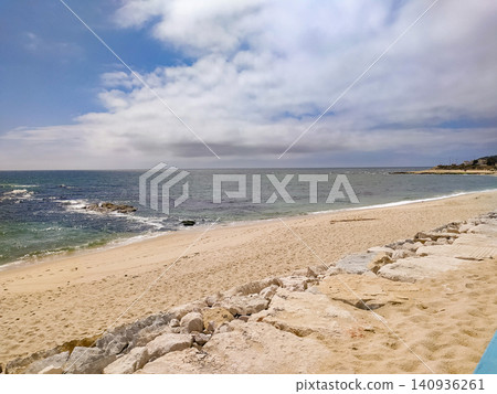 An idyllic, empty sandy beach stretches under a beautiful, cloudy blue sky. With nobody around, the calm ocean waves and rocky shore evoke peaceful vibes of a scenic summer escape. An idyllic, empty sandy beach stretches under a beautiful, cloudy blue sky. With nobody around, the calm ocean waves and rocky shore evoke peaceful vibes of a scenic summer escape. 140936261