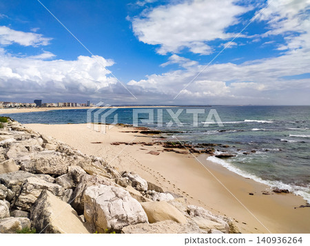 A peaceful coastal landscape with a rocky shoreline, golden sand beach, and blue ocean waves under a cloudy sky. Nobody is here, evoking serene tranquility, ideal for travel designs. A peaceful coastal landscape with a rocky shoreline, golden sand beach, and blue ocean waves under a cloudy sky. Nobody is here, evoking serene tranquility, ideal for travel designs. 140936264