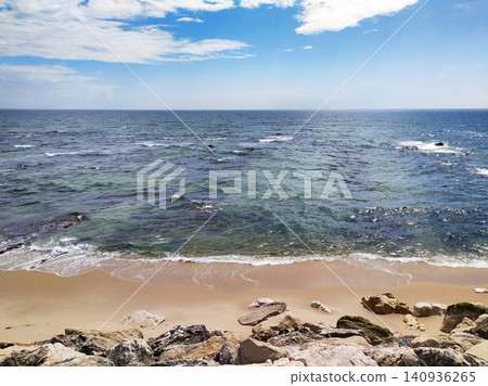 A tranquil and sunny ocean beach with rocks under a blue sky, evoking a sense of peaceful solitude and natural beauty. This scenic seascape features nobody, perfect for travel. 140936265