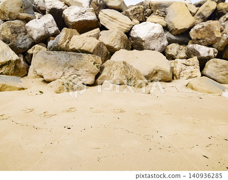 A peaceful sandy beach meets a sturdy wall of massive, weathered coastal rocks. This natural, textured background evokes a feeling of calm and solid protection. Nobody present. A peaceful sandy beach meets a sturdy wall of massive, weathered coastal rocks. This natural, textured background evokes a feeling of calm and solid protection. Nobody present. 140936285
