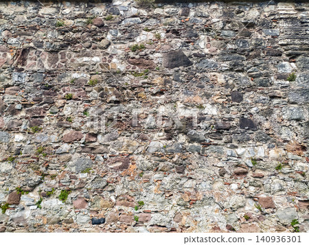 An ancient, rustic stone wall texture background showing weathered rocks and small green plants growing in crevices. Nobody. Evokes feelings of history, strength, and timeless endurance. 140936301