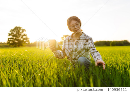 Young woman agronomist works on a modern digital tablet on a green wheat field. Young woman agronomist works on a modern digital tablet on a green wheat field. 140936511