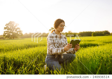 Young woman agronomist works on a modern digital tablet on a green wheat field. Young woman agronomist works on a modern digital tablet on a green wheat field. 140936514