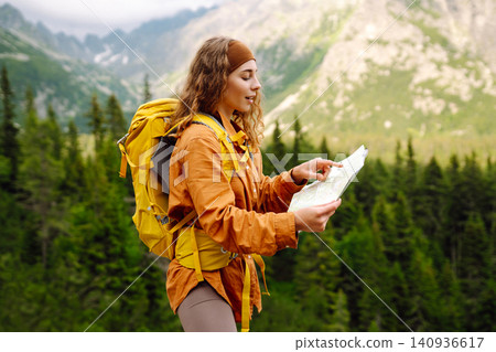 Woman traveler holds a map, explores hiking trails in the mountains. Hiking and adventure concept Woman traveler holds a map, explores hiking trails in the mountains. Hiking and adventure concept 140936617
