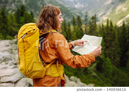Woman traveler holds a map, explores hiking trails in the mountains. Hiking and adventure concept Woman traveler holds a map, explores hiking trails in the mountains. Hiking and adventure concept 140936618