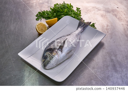 Sea bream fish on a white plate with parsley and lemon Sea bream fish on a white plate with parsley and lemon 140937446