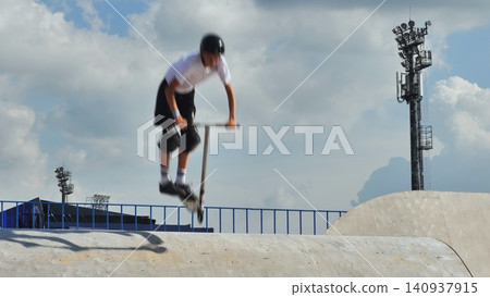 Young boy performing extreme scooter jump trick in skatepark halfpipe action Young boy performing extreme scooter jump trick in skatepark halfpipe action 140937915