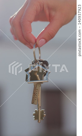 Vertical video A hand with a keychain in the shape of a small house and keys against the background of house. 140937923