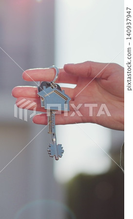 Vertical video Key ring with keychain house in hand on background of house. Real estate concept for buying a new home. Vertical video Key ring with keychain house in hand on background of house. Real estate concept for buying a new home. 140937947
