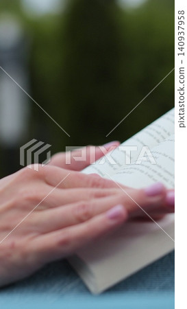 Vertical video Close-up of a woman hand turning to a new page in the backyard of a house. Vertical video Close-up of a woman hand turning to a new page in the backyard of a house. 140937958