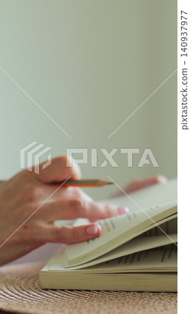 Vertical video Close-up woman student preparing her lessons at an office table. The girl reads and studies from an book and takes notes with a pencil. The young woman studies at home. 140937977
