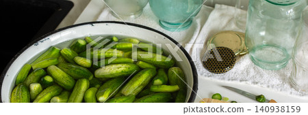 Cucumbers are soaking in a bowl while garlic and cucumber slices are on a cutting board. Several empty jars sit nearby on a clean countertop. It is a preparation activity for winter storage, banner Cucumbers are soaking in a bowl while garlic and cucumber slices are on a cutting board. Several empty jars sit nearby on a clean countertop. It is a preparation activity for winter storage, banner 140938159