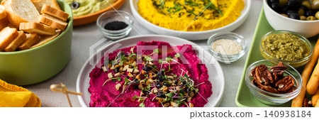 A colorful charcuterie board features beetroot hummus, classic hummus, broccoli hummus, and turmeric hummus, garnished with toppings, surrounded by bread and olives, banner A colorful charcuterie board features beetroot hummus, classic hummus, broccoli hummus, and turmeric hummus, garnished with toppings, surrounded by bread and olives, banner 140938184