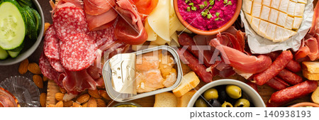 Enjoy a vibrant charcuterie board filled with assorted cheeses, savory sausages, creamy hummus, nuts, and colorful vegetables. Perfect for sharing at a casual gathering, banner Enjoy a vibrant charcuterie board filled with assorted cheeses, savory sausages, creamy hummus, nuts, and colorful vegetables. Perfect for sharing at a casual gathering, banner 140938193