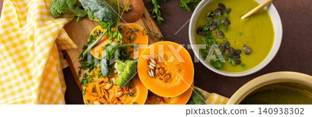 A table displays bowls of pumpkin soup with broccoli topped with seeds and herbs. Nearby, fresh ingredients and a pot hold more soup, creating a healthy meal setting, banner A table displays bowls of pumpkin soup with broccoli topped with seeds and herbs. Nearby, fresh ingredients and a pot hold more soup, creating a healthy meal setting, banner 140938302