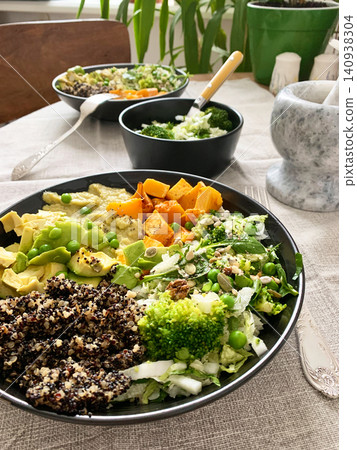 A bowl filled with quinoa, roasted pumpkin, hummus, and a salad of fresh avocado is ready to eat. This meal is gluten free and offers a healthy start to the day 140938304