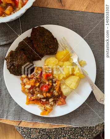 A plate holds liver pancakes next to boiled potatoes and a colorful fresh salad. The meal is served on a table with a simple cloth, perfect for breakfast or lunch A plate holds liver pancakes next to boiled potatoes and a colorful fresh salad. The meal is served on a table with a simple cloth, perfect for breakfast or lunch 140938307