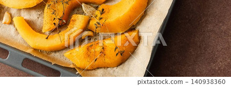Butternut squash slices are arranged on a tray with herbs and garlic, ready for roasting. This is part of a cooking process in a kitchen setting, banner Butternut squash slices are arranged on a tray with herbs and garlic, ready for roasting. This is part of a cooking process in a kitchen setting, banner 140938360