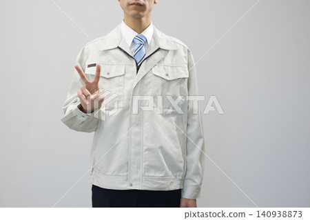 A young man in work clothes makes a V-sign. A young man in work clothes makes a V-sign. 140938873