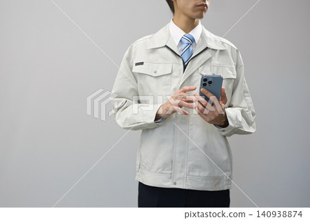 A young man in work clothes holding a smartphone A young man in work clothes holding a smartphone 140938874