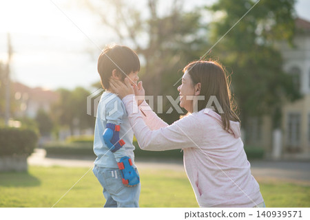 Happy Asian mother gently holding her young son's face and smiling together at the park during beautiful golden hour sunset. Happy Asian mother gently holding her young son's face and smiling together at the park during beautiful golden hour sunset. 140939571