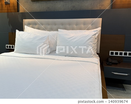 Hotel bed with white sheets and pillows in a modern room, creating a cozy and inviting background Hotel bed with white sheets and pillows in a modern room, creating a cozy and inviting background 140939674