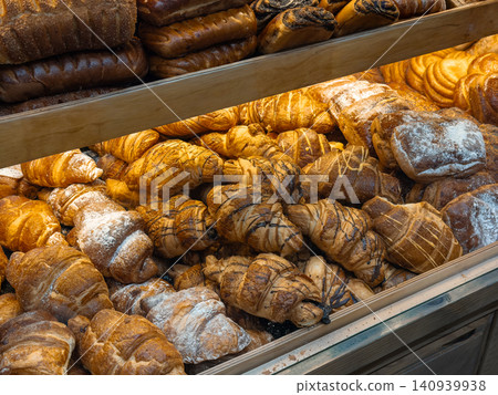 Freshly baked buttery croissants and assorted pastries arranged in rows on display shelves at a rustic bakery store, creating an inviting atmosphere for delicious breakfast treats Freshly baked buttery croissants and assorted pastries arranged in rows on display shelves at a rustic bakery store, creating an inviting atmosphere for delicious breakfast treats 140939938