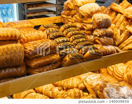 Assorted fresh pastries and golden loaves of bread arranged on wooden shelves in a bakery shop, displaying a variety of delicious baked goods for sale in a warm inviting display Assorted fresh pastries and golden loaves of bread arranged on wooden shelves in a bakery shop, displaying a variety of delicious baked goods for sale in a warm inviting display 140939939