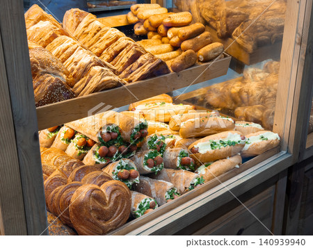 Assorted fresh pastries and hot dog sandwiches displayed on rustic wooden shelves at a local bakery shop, capturing the appetizing atmosphere of a small food business for hungry Assorted fresh pastries and hot dog sandwiches displayed on rustic wooden shelves at a local bakery shop, capturing the appetizing atmosphere of a small food business for hungry 140939940