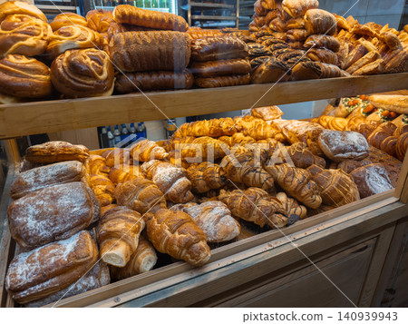 Assorted fresh pastries and bread loaves arranged on shelves in a bakery display case, conveying a warm artisan atmosphere and appetizing variety for breakfast or dessert service 140939943